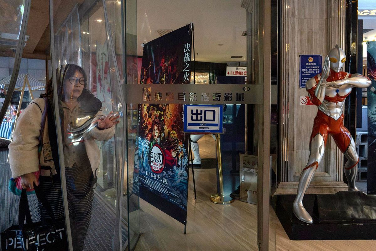 日本のアニメのポスターやウルトラマンのフィギュアが展示された北京の映画館の前を通る女性/Ng Han Guan/AP via CNN Newsource