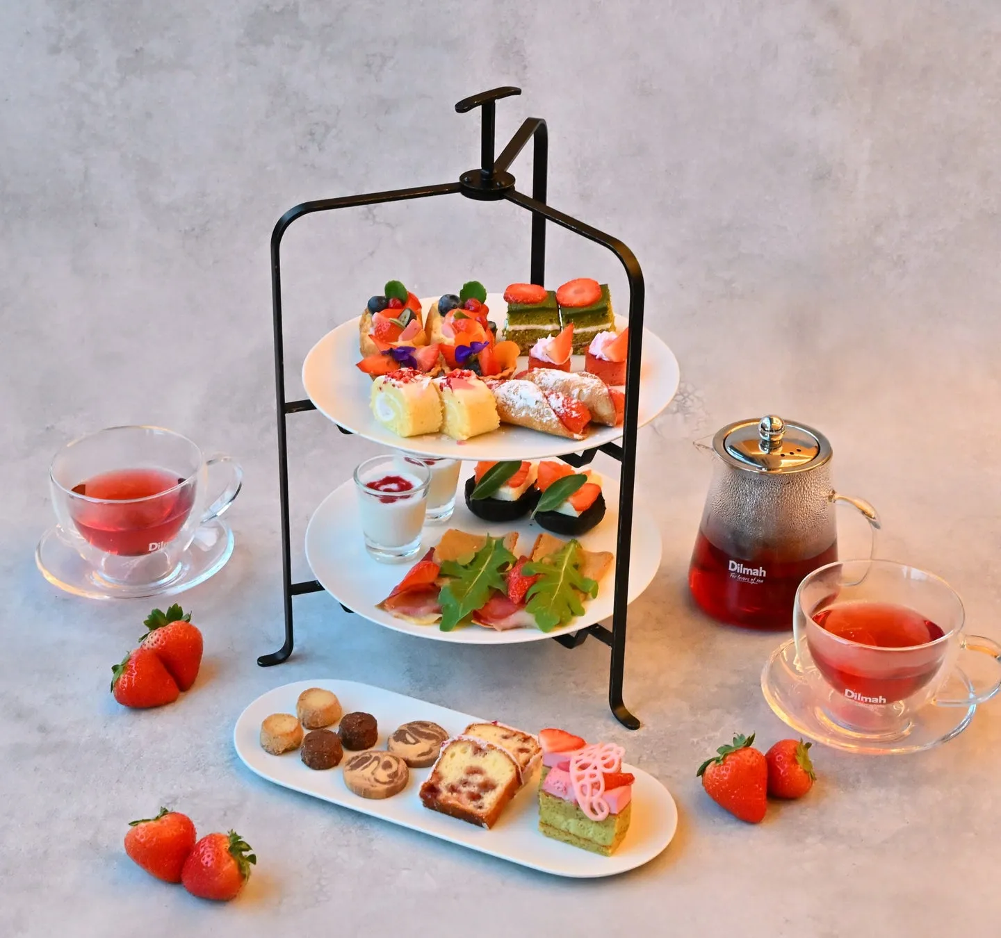 アフタヌーンティーセットの画像。3段のケーキスタンドには、様々な種類のケーキやデザートが並べられ、イチゴやクッキー、紅茶のポット、ティーカップも添えられています。