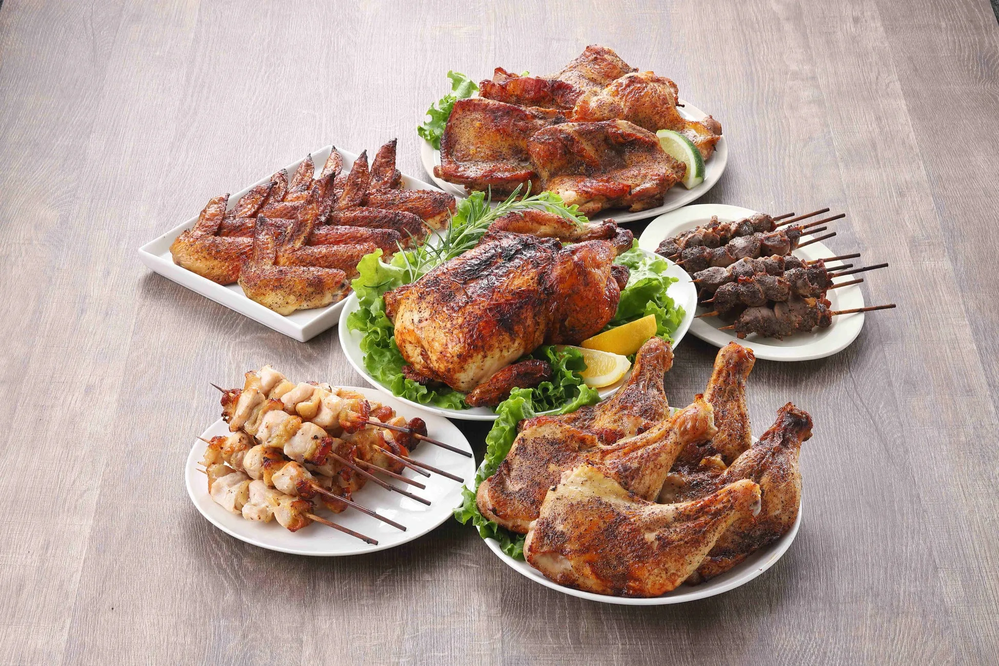 様々なお肉料理が並んだ写真です。ローストチキン、鶏肉のグリル、串焼きなど、食欲をそそる料理が白いお皿に盛り付けられています。