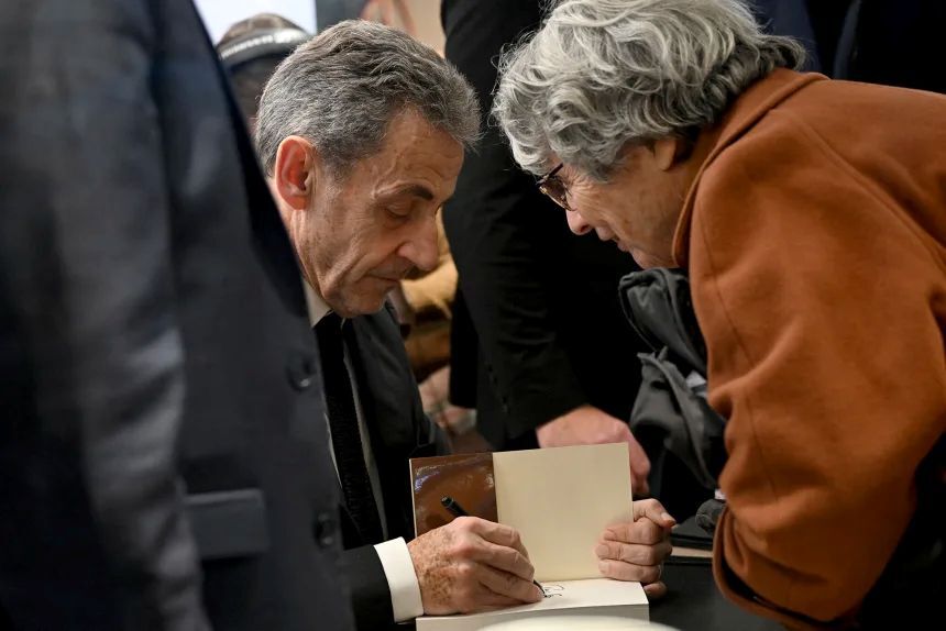 読者が購入した自身の著書にサインするサルコジ氏/Bertrand Guay/AFP/Getty Images
