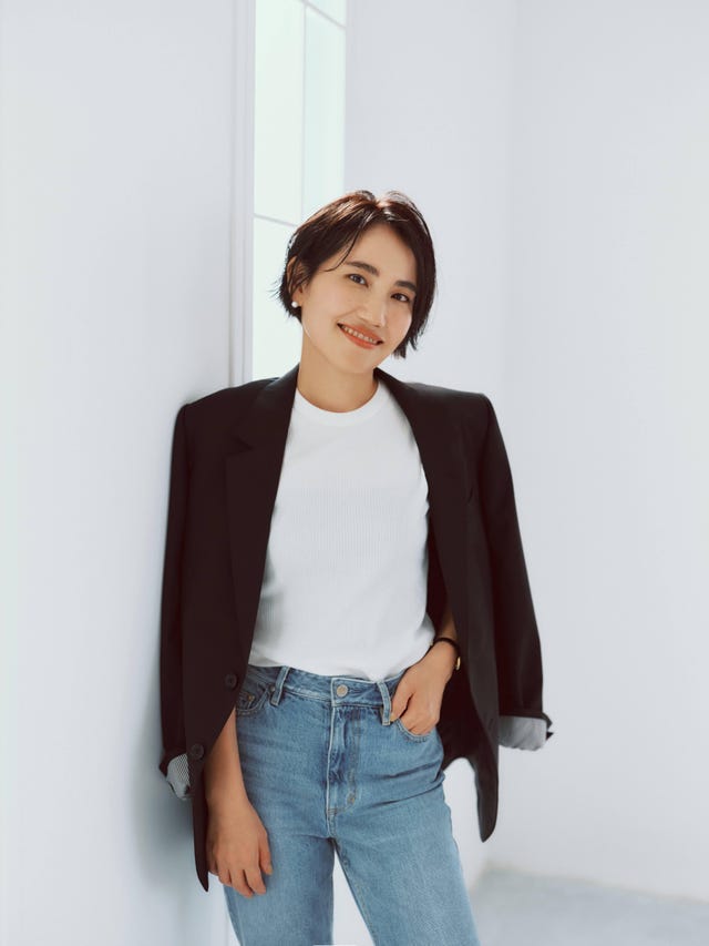 a person wearing a black blazer and white top standing in a bright minimalist space a person wearing a black blazer and white top standing in a bright minimalist space