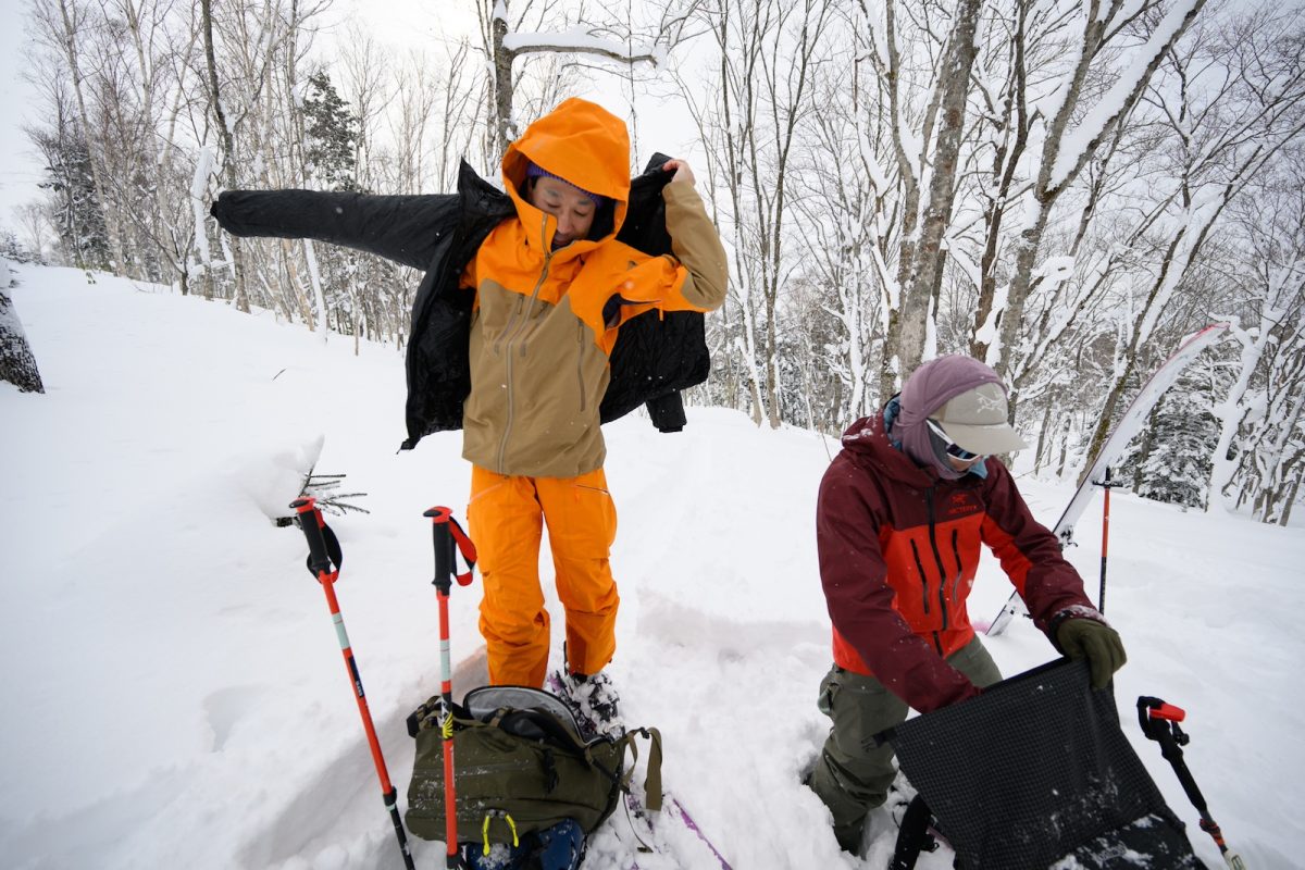 ハイクの休憩中、シェルの上からオーバーレイヤー（ダウン）を羽織り、冷えから身を守る。