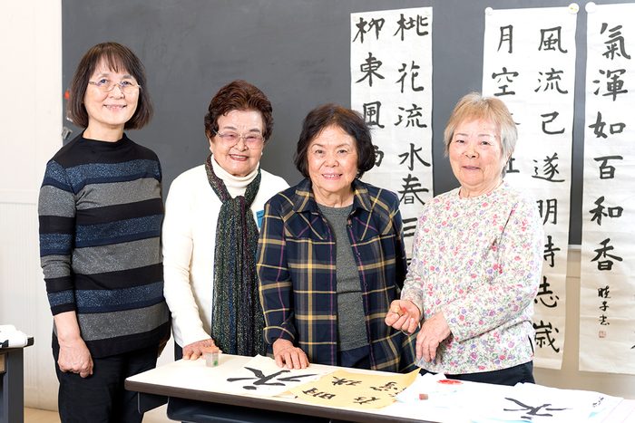 書道クラブ員が師事する、龍賓沖縄書道会師範の大田春翠（安子）さん（左から3人目）。学習発表会を控えて完成した作品に落款印を押す。書道クラブ員（左から）棚原睦子さん、安里貞子さん、東江アヤさん（右端）
