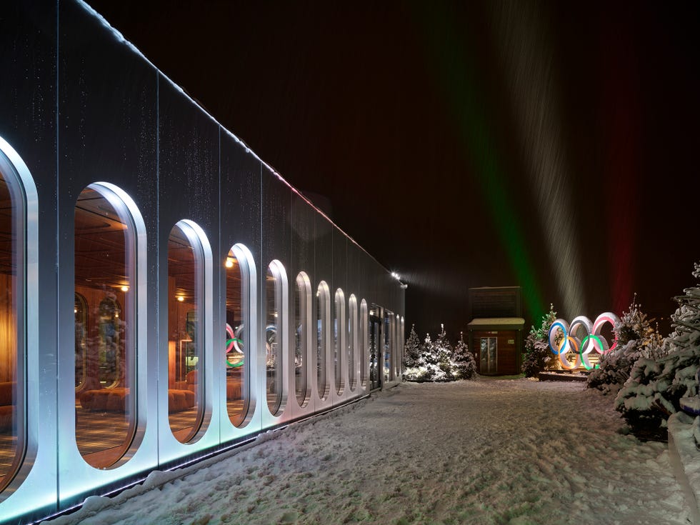 照明付きアーチと雪景色を背景に、五輪を掲げた近代的なコルティナのカーザ・イタリアの建物外観。