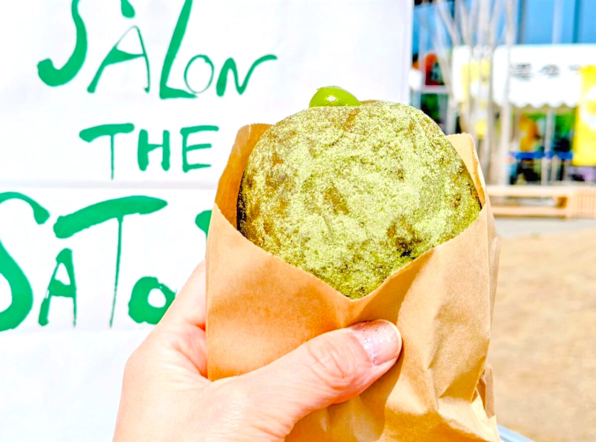 静岡県牧之原市・道の駅 そらっと牧之原「さとりベーカリー」お濃茶クリーム生ドーナツ 手に持って看板とのショット