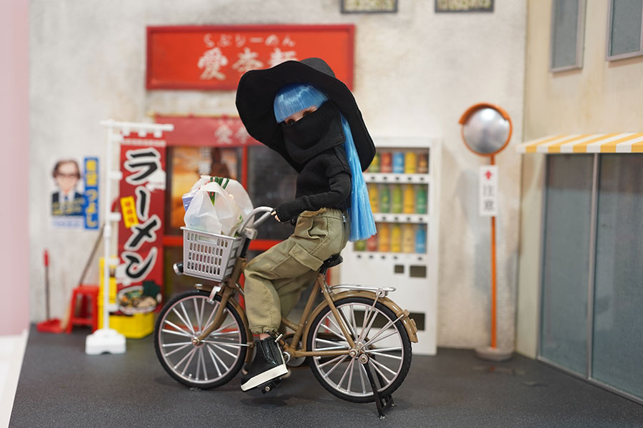 架空のラーメン店「愛李麺」の前で、紫外線をガードした服装で、ママチャリに乗るインフルエンサー（2月3日撮影／Lmaga.jp）