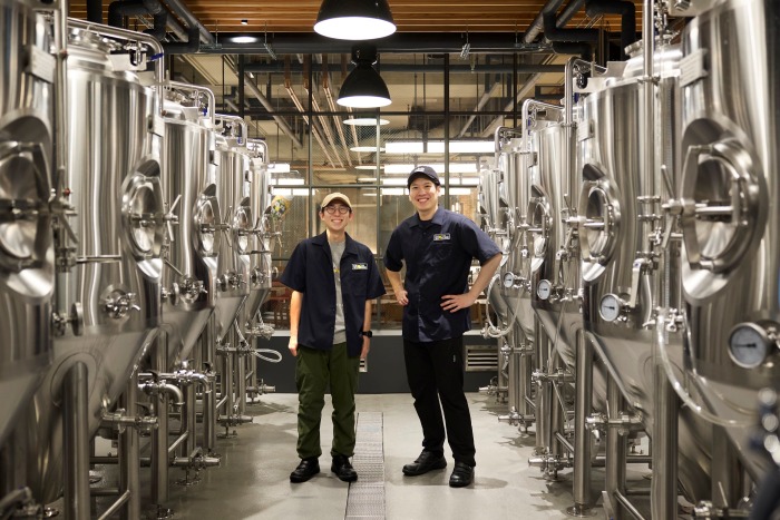 YONA YONA TOKYO BREWERY醸造所のタンクの間にブルワー2名が立っている様子