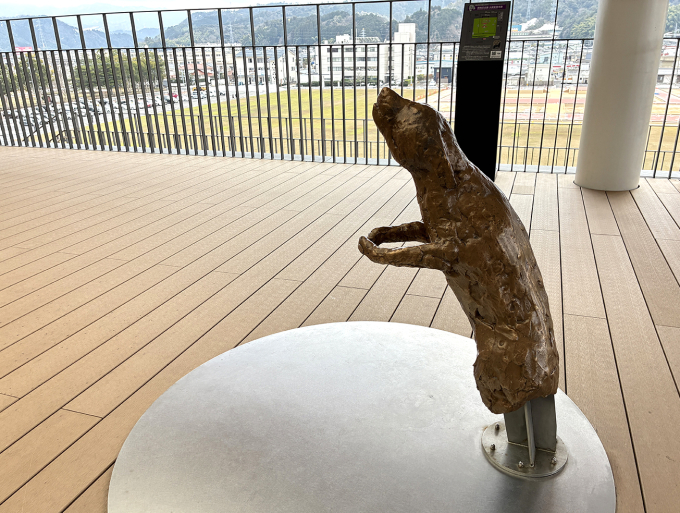 展望テラスには、中ハシ克シゲによる触ることができる彫刻《お出掛け犬》《抱きつき犬》も設置されている。写真の《抱きつき犬》は、犬が足に飛びついた様子を現しており、犬の前足の輪の中に足を入れ、なでながら鑑賞ができる。