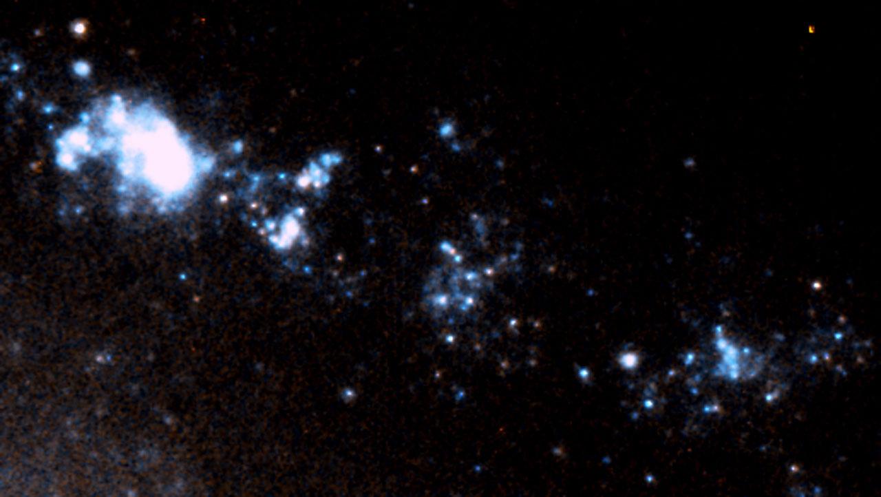 ぼうえんきょう座の方向約1億2000万光年先にある棒渦巻銀河「ESO 184-G82」の一部を拡大した擬似カラー画像。星形成領域である青白い水素ガス複合体が帯状に広がっている。この領域内に、1998年に発生したガンマ線バースト「GRB 980425」および超新星「SN 1998bw」の残光とみられる、ひときわ明るくコンパクトな光源がはっきりと捉えられている（Credit: ESA, Stephen Holland (Danish Centre for Astrophysics with the HST), Jens Hjorth, Johan Fynbo (University of Copenhagen)）