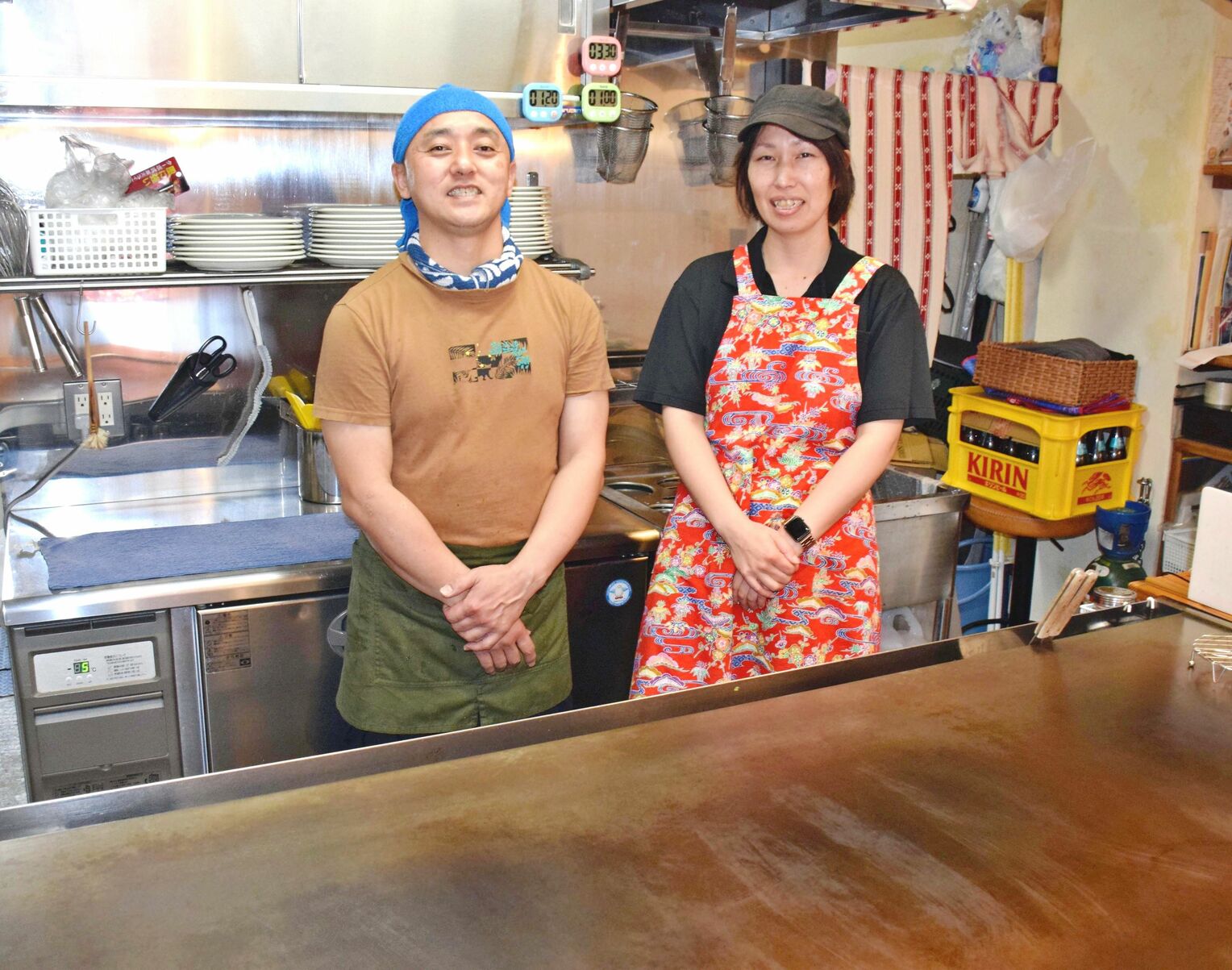 広島お好み焼き５４の佐藤貴彦さん（左）、美那子さん夫妻。カウンターは鉄板の上で熱々のまま食べることもできる＝５日、嘉手納町嘉手納