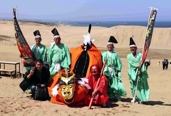 雄大な砂丘をバックに麒麟獅子と記念撮影する観光客ら