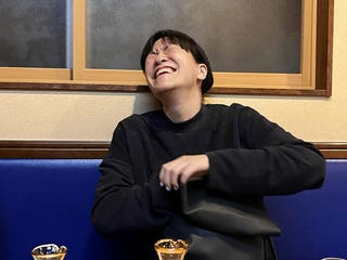 person seated at a table with drinks and a bag