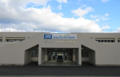 全体がクリーム色の外壁で「東北ヒロセ陸上競技場」と書かれた看板が正面の壁に設置されている玄関入口前の外観写真