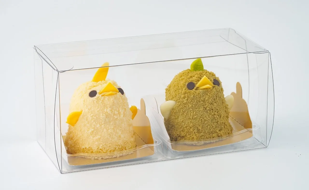 透明なケースに入った、ひよこの形をした可愛いケーキの写真です。黄色と緑色の2種類のケーキが並んでおり、それぞれ異なる表情をしています。