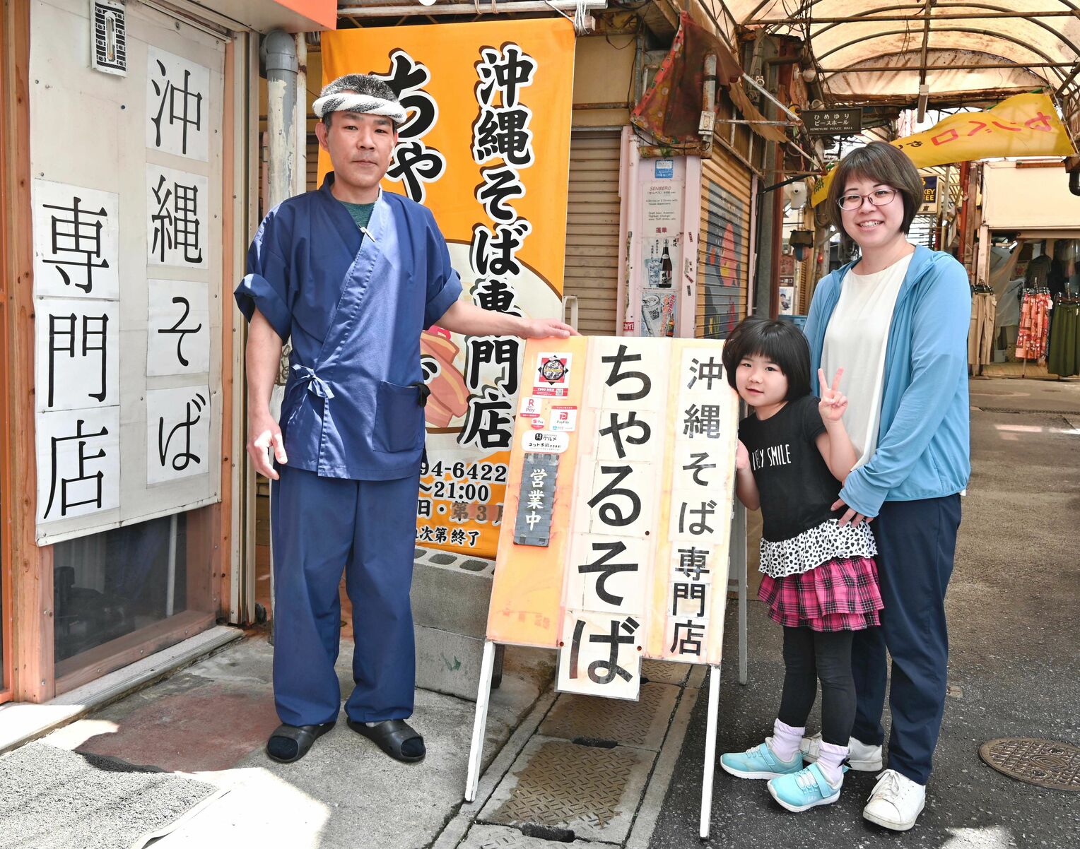 栄町市場内で店を構える店主の宮城春之さん（左）と妻の加七子さん（右）、娘の七華さん＝１１日、那覇市安里