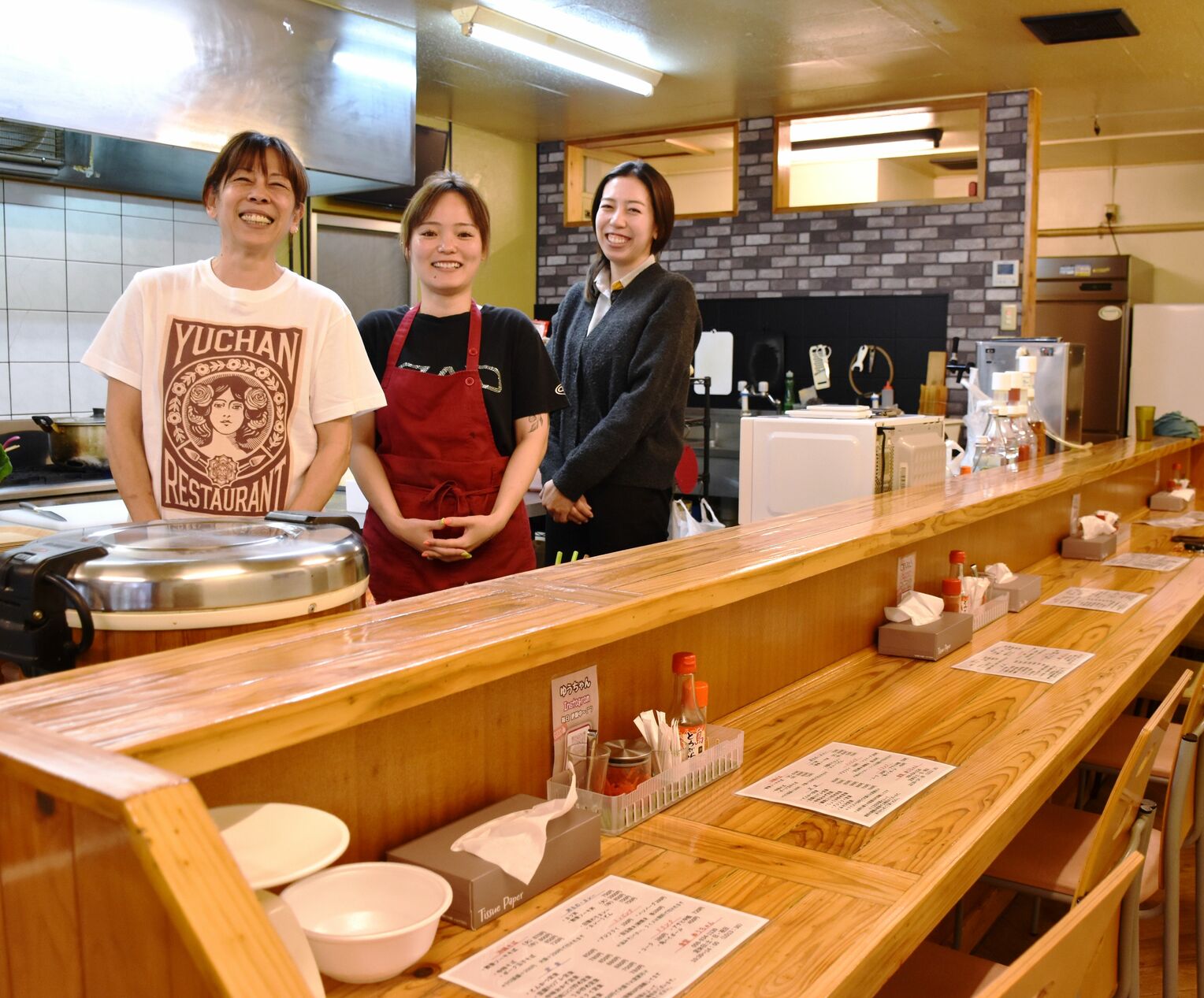 笑顔でオープンキッチンに立つ（左から）知念優子さんと次女の舞さん、三女の結菜さん＝７日、沖縄市胡屋の「ゆうちゃん弁当」