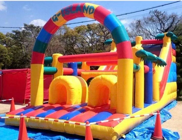 G-ISLANDロゴ入りの大型インフレータブルアスレチック遊具。赤・黄・青・緑の多色トンネル型バウンサーで、イベント会場の子ども向けアトラクションとして設置