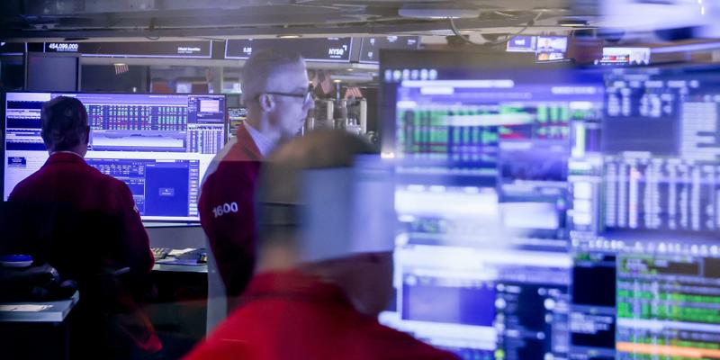 Traders at the New York Stock Exchange looking at monitors from behind a glass