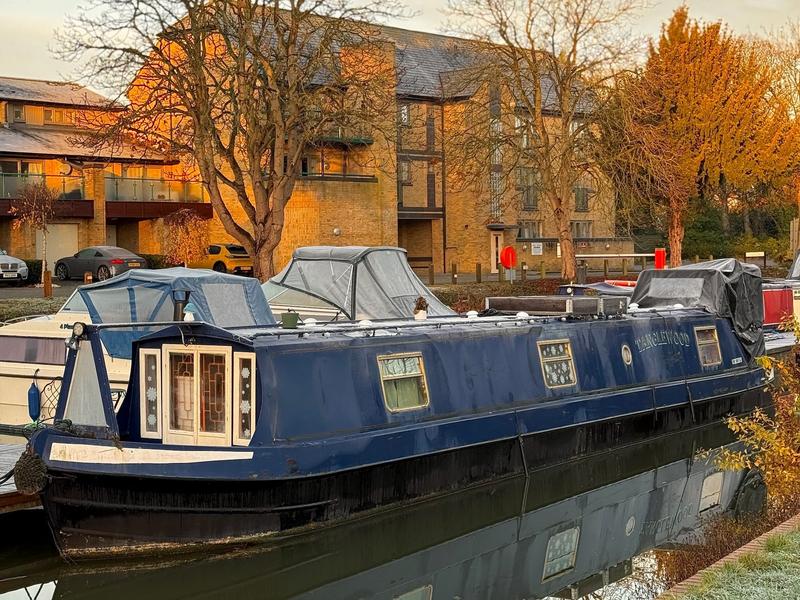 A blue boat on a river in front of an apartment building.