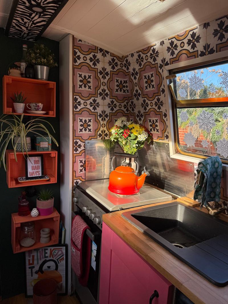 A kitchen inside a narrowboat with a patterned tile wall and a small stove.