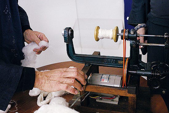 spinning machine being operated to spin fibers into yarn　いしげ結城紬の糸作り