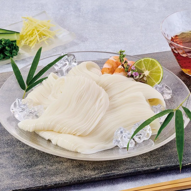 ガラスの皿に盛り付けられた冷やしそうめん。薬味として、きゅうり、生姜、エビ、ライムが添えられている。氷も添えられ、涼しげな印象を与える。