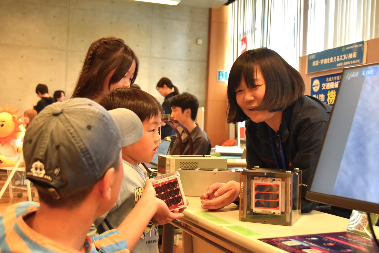 超小型人工衛星の模型で説明する宮田准教授（右）
