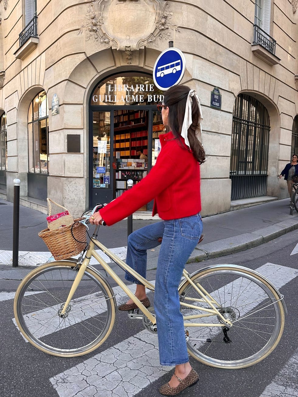 bicyclist in a red jacket with a basket near a bookstore