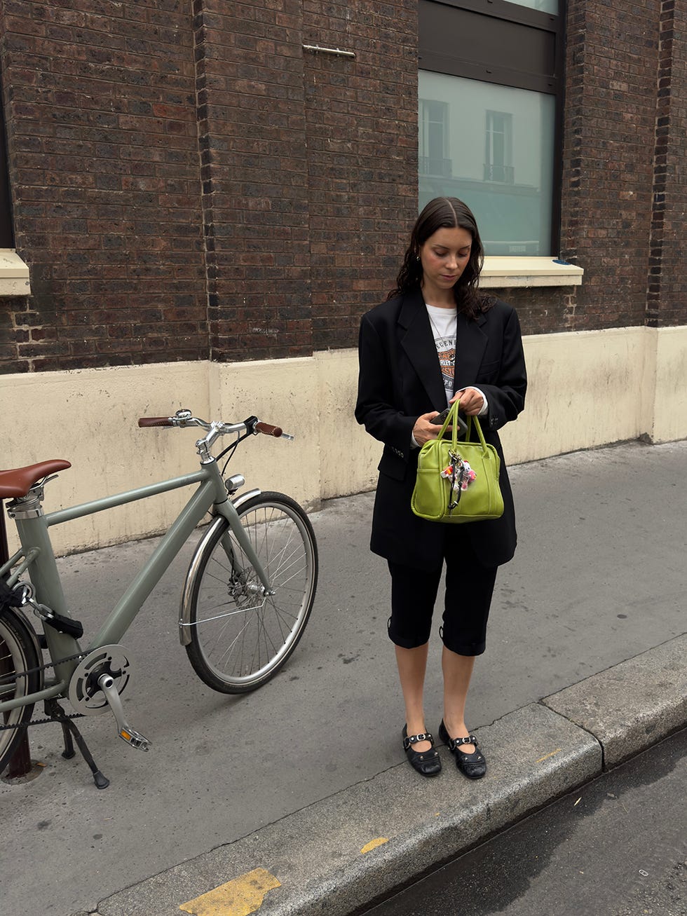 person standing on a city street next to a bicycle holding a green handbag