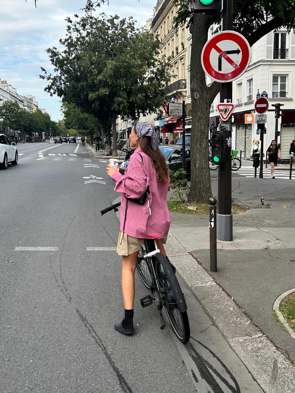 person standing next to a bicycle in an urban setting holding a drink
