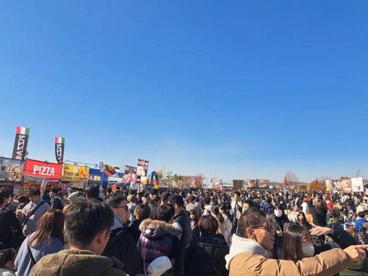 青空の下、全肉祭会場に大勢の来場者が集まった過去開催の野外グルメイベント会場風景。PIZZA・牡蠣などの出店旗と混雑した通路が写る