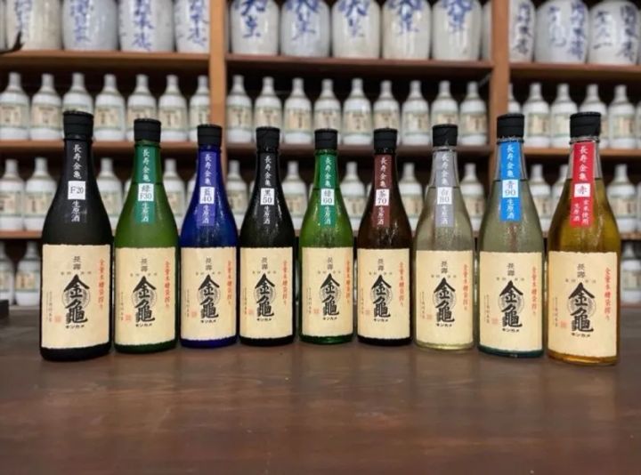 長寿金亀シリーズの精米歩合別9本（F20〜赤）を一列に並べた商品比較写真。各瓶のラベル色・精米歩合表記が判別できる酒蔵の商品ラインナップ紹介ショット