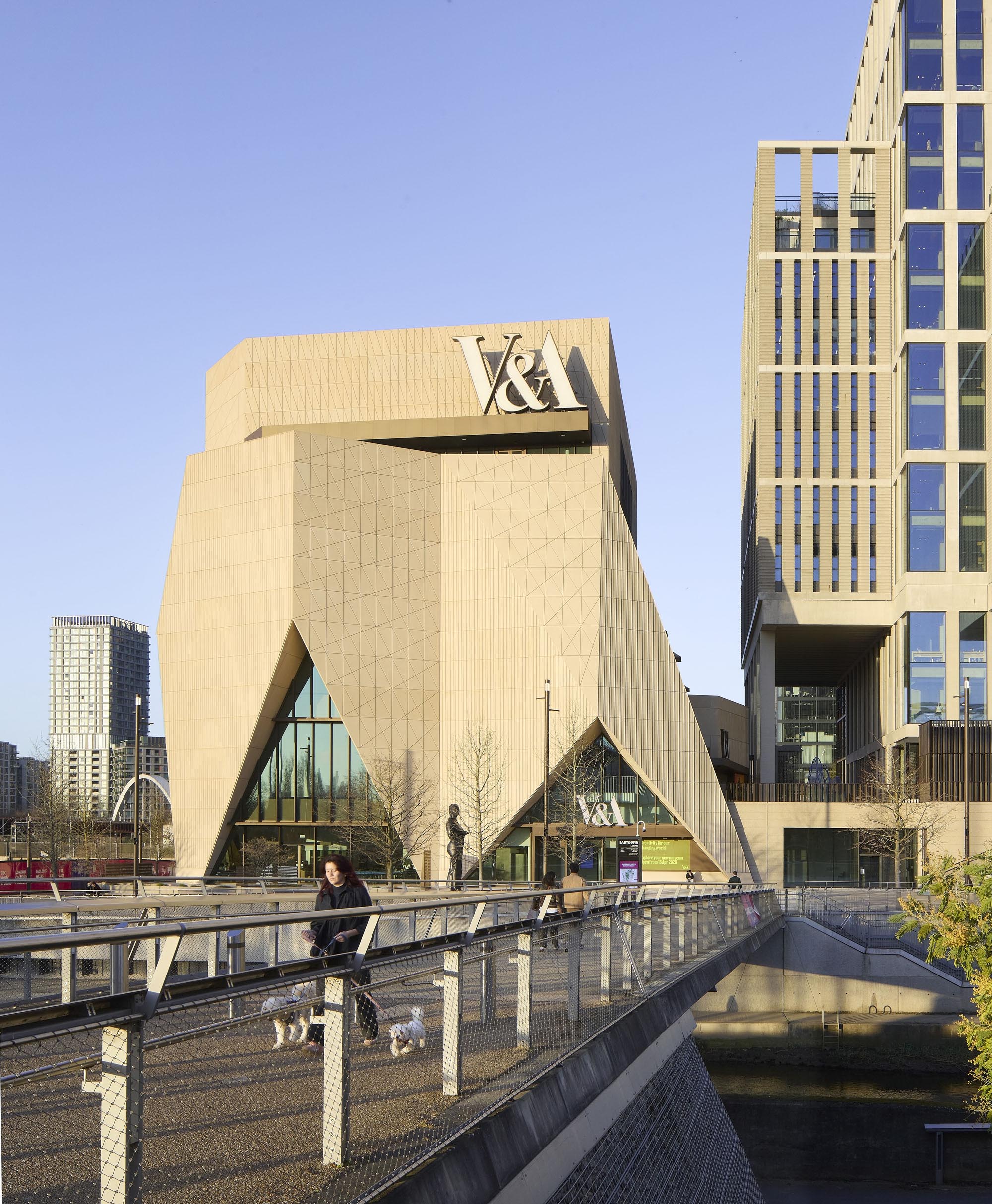 V&A museum building with angular beige facade beside a pedestrian bridge on a sunny day