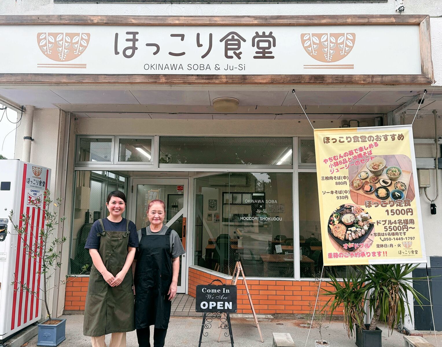 笑顔で店前に立つ中能真梨さん(左)と與古田枝梨子さん=8日、沖縄市松本・ほっこり食堂