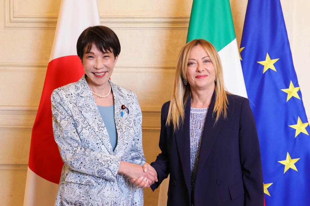 日本国旗、イタリア国旗およびEU旗を背に、笑顔で握手を交わす高市総理大臣とメローニ首相