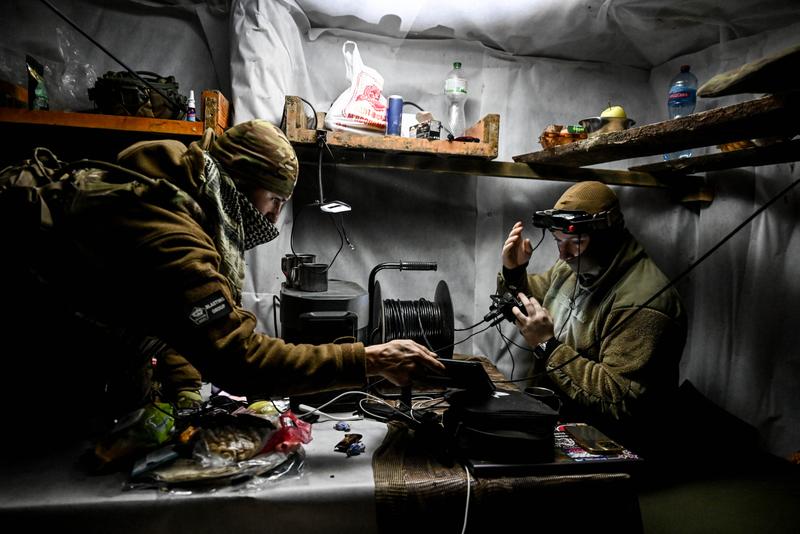 Two men in khaki in an indoor location with controllers and fiber optic spools