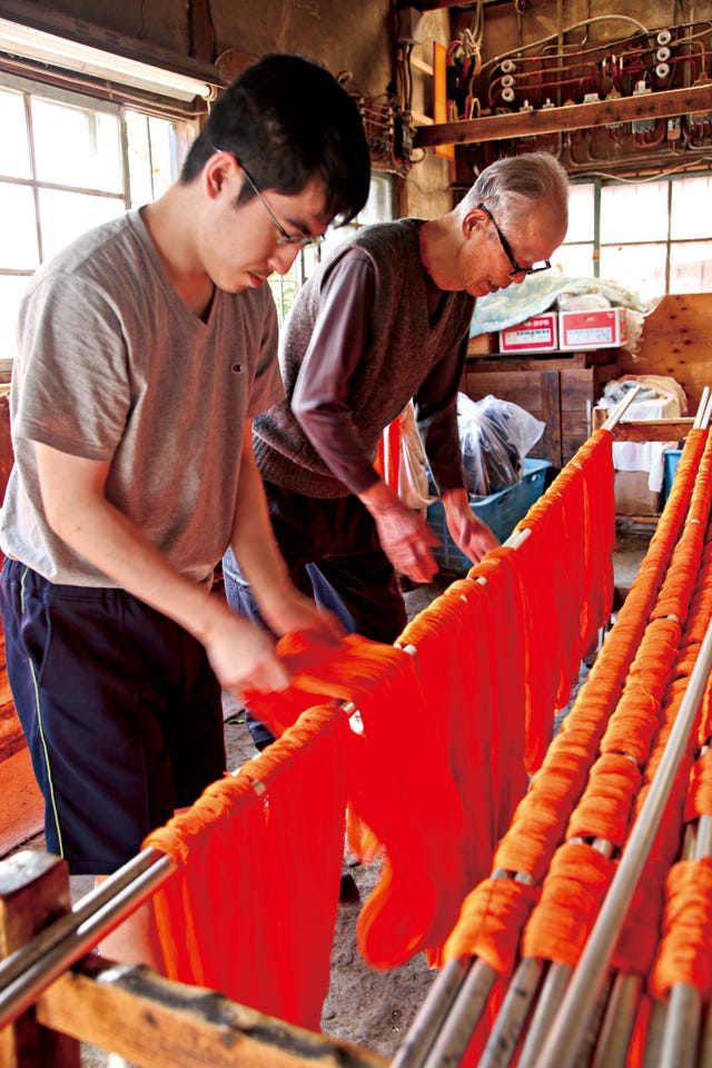 two individuals working with bright orange strands in a textile workshop