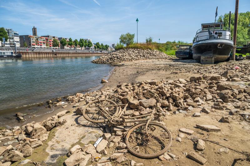 A mud-covered bike and stranded houseboat lay on a dried riverbed.