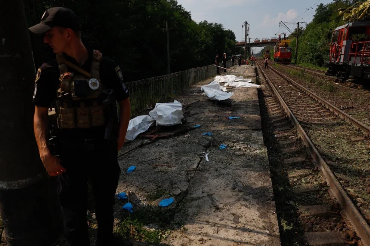 ロシアの弾道ミサイルやドローン攻撃で死亡し、プラスチック製の袋に収容された遺体のそばに立つ警察官=5日、キーウ州の鉄道駅/Mykola Tymchenko/AFP/Getty Images