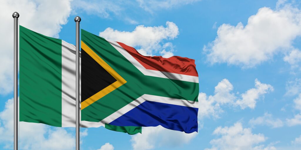 Nigeria and South Africa flag waving in the wind against white cloudy blue sky together. Diplomacy concept, international relations. | NADA NEWS(ナダ・ニュース) Nigeria and South Africa national flags fluttering on flagpoles against a blue sky, side by side.