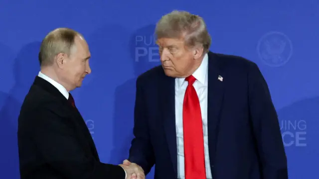 青い背景の記者会見場で握手を交わすプーチン氏とトランプ氏