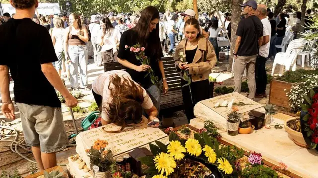 墓地で墓に顔を寄せる人や、花を手に立っている人たちがいる