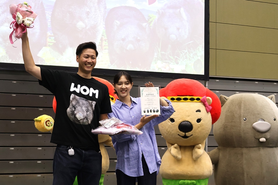 「ウォンバット課（自称）」から贈呈された花束を掲げる坂本さん・芳谷さんカップル（10月18日撮影、五月山体育館）
